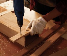 Carpenter using drill to screwing pieces of board at site.